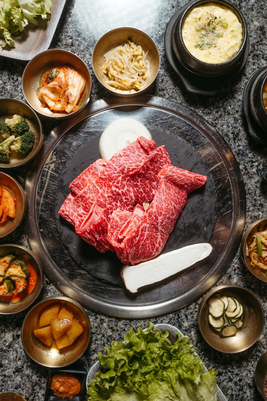 Sliced marinated beef on a grill plate surrounded by small side dishes