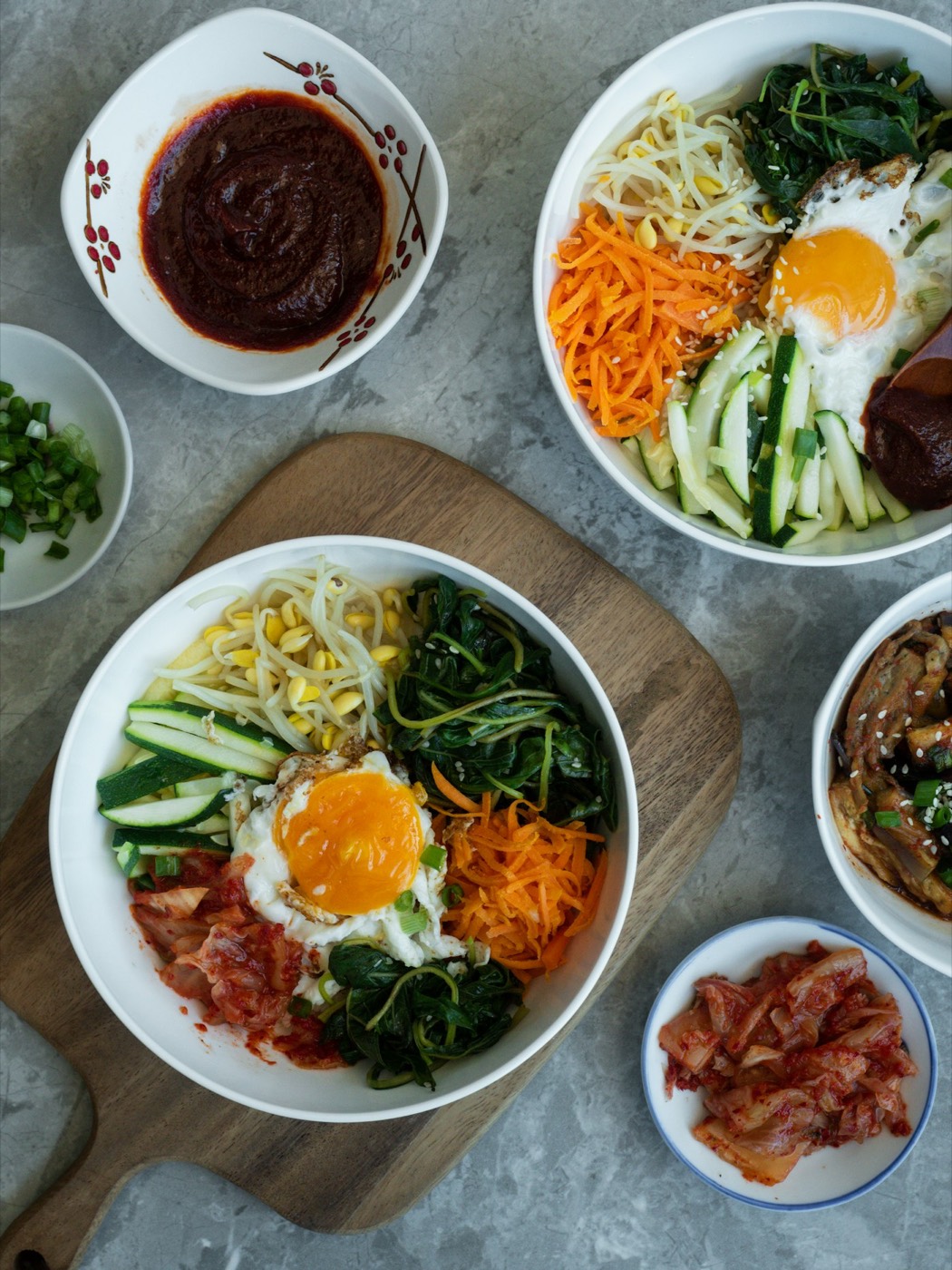 Two bowls of bibimbap with gochujang on the side